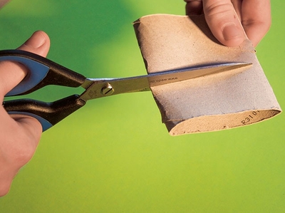 Hand schneidet mit Schere eine Papierrolle auf grünem Untergrund.
