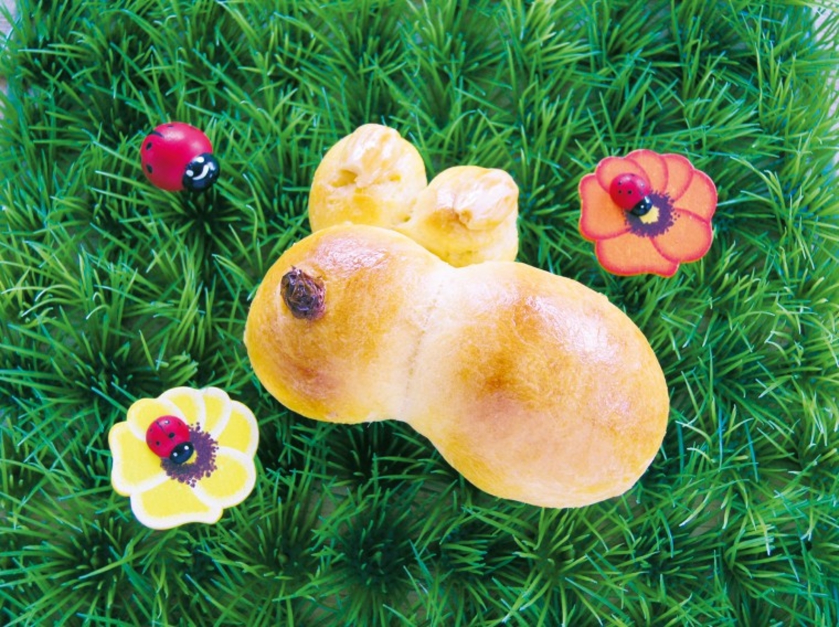 Fertig gebackene Osterhasen aus Teig auf grünem Untergrund, dekoriert mit Blumen.