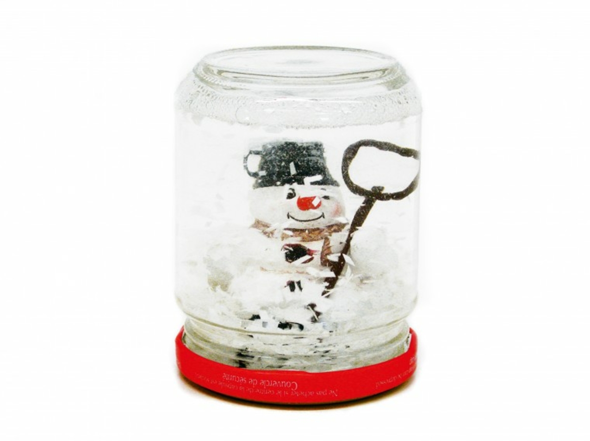 Selbstgebastelte Schneekugel im Glas mit Schneemannfigur und rotem Deckel.